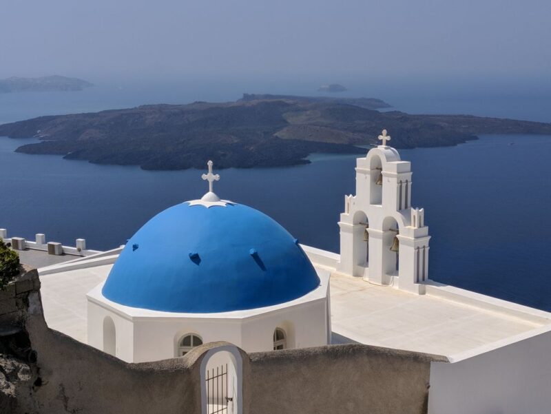 Santorini, Greek island accessible by plane: white church with blue roof and view of the Caldera